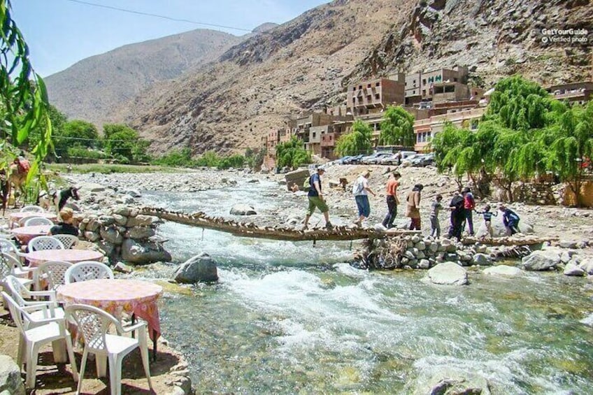 A river crossing with people walking and a restaurant with outdoor seating. 3