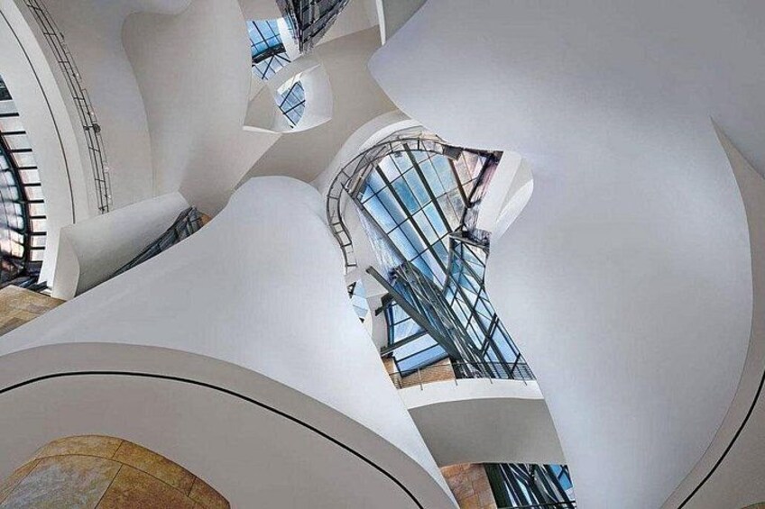 Un intérieur architectural moderne avec des murs blancs aux lignes courbes, des rampes en verre et un escalier central. 4