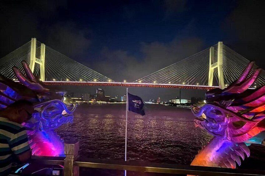 Vista nocturna de un puente iluminado con dos esculturas de dragones iluminados sobre una barca. 5