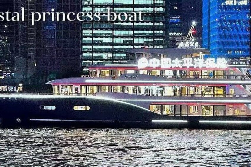 Un bateau fluvial aux hublots illuminés et au toit rouge est amarré à un quai, avec une vue sur la ville en arrière-plan. 3