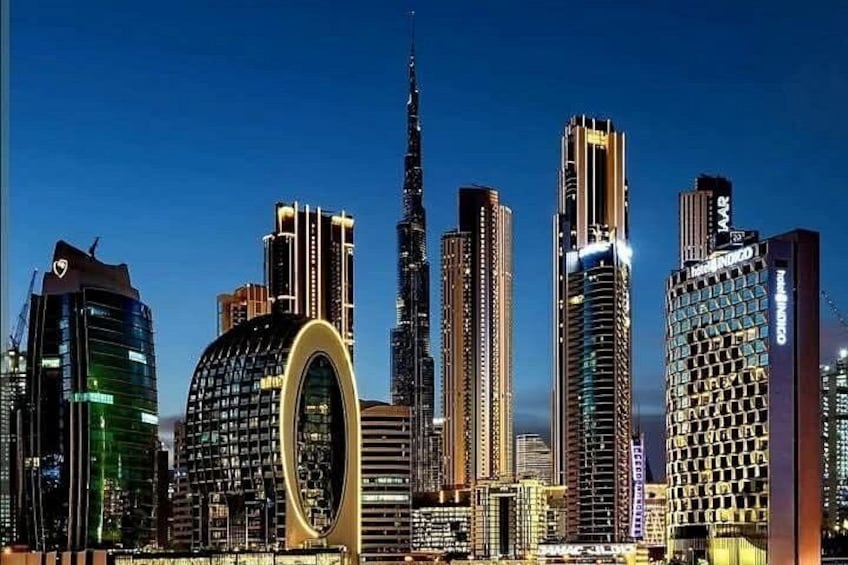Un horizonte urbano al atardecer con edificios iluminados, incluyendo una estructura curva distintiva y varias torres altas. 1