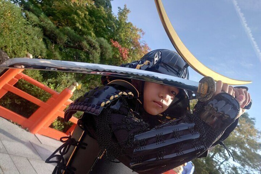A person in traditional samurai armor holding a curved sword, standing in front of a torii gate. 5