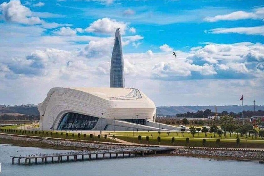 A modern architectural structure with a unique curved design, a tall central tower, and a waterfront setting. 1
