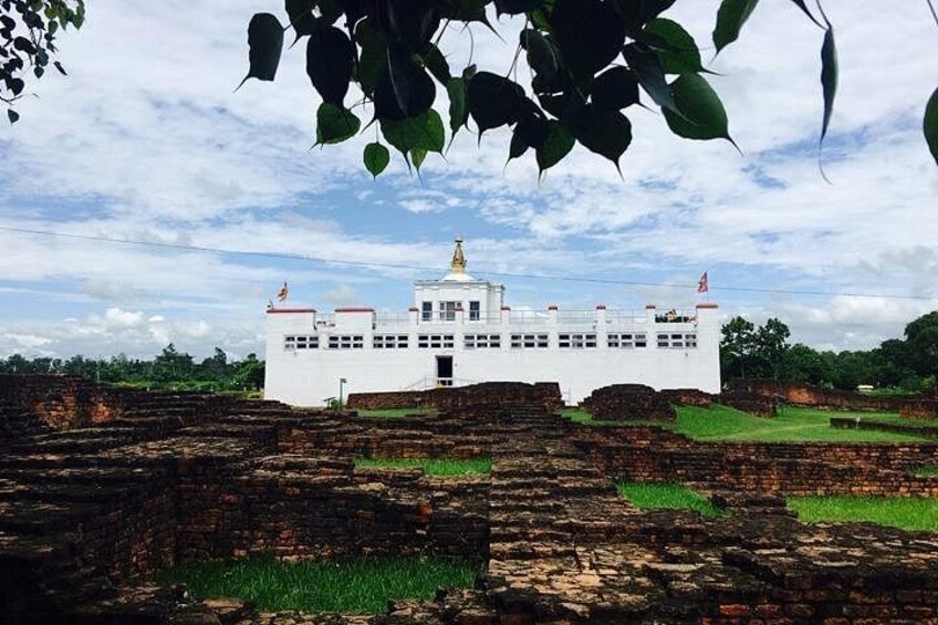 A white building with a golden spire, surrounded by ancient brick ruins and greenery. 2