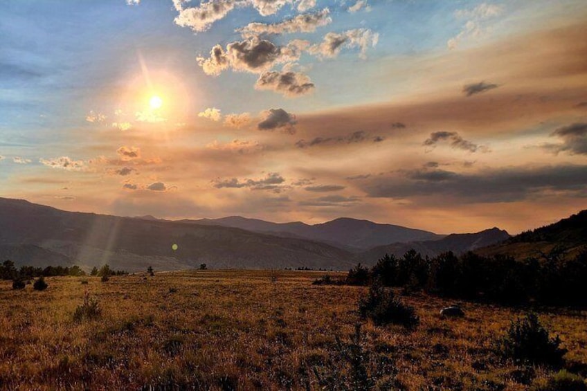 Un atardecer sobre un campo cubierto de hierba con montañas al fondo. 5