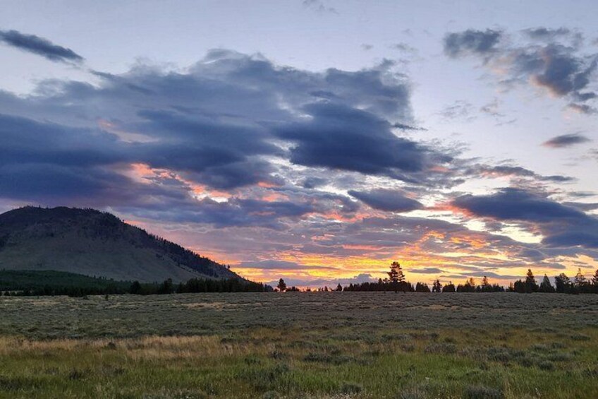 Un atardecer sobre un campo de hierba con una colina al fondo. 2