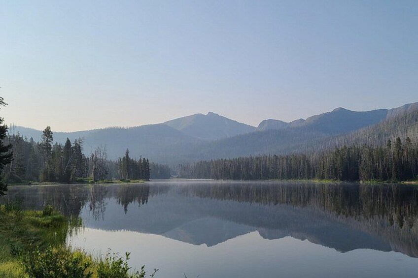 Un lago tranquilo con montañas al fondo y un bosque denso a la izquierda. 1