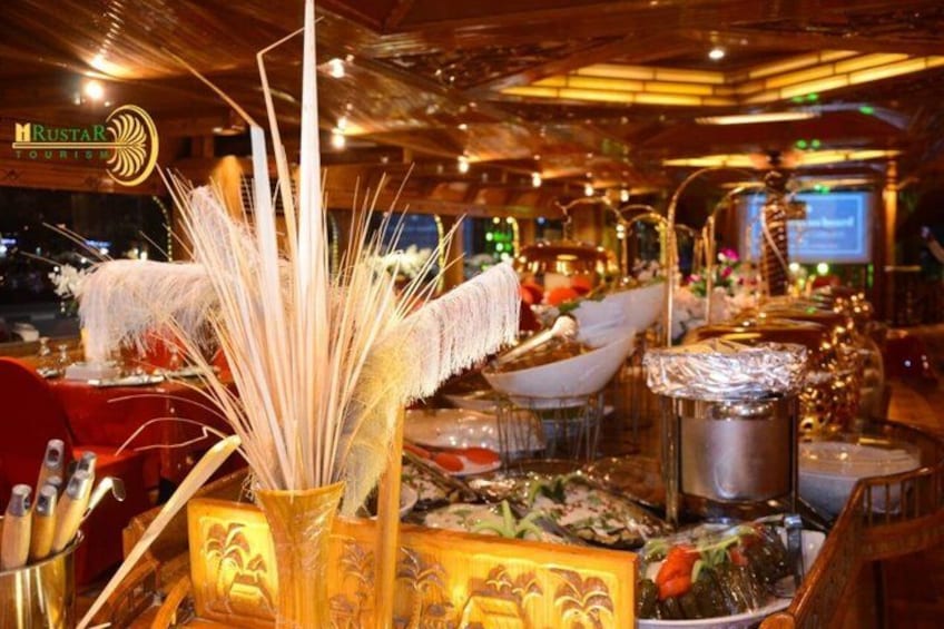 A restaurant interior with a warm ambiance, featuring a decorative centerpiece with tall grasses and a golden vase, a wooden ceiling, and a sign that reads 'MUSTAR TOURISM'. 2