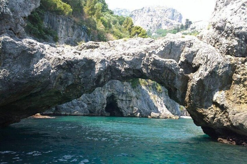 A natural rock arch formation over turquoise water, surrounded by rugged cliffs and greenery. 3