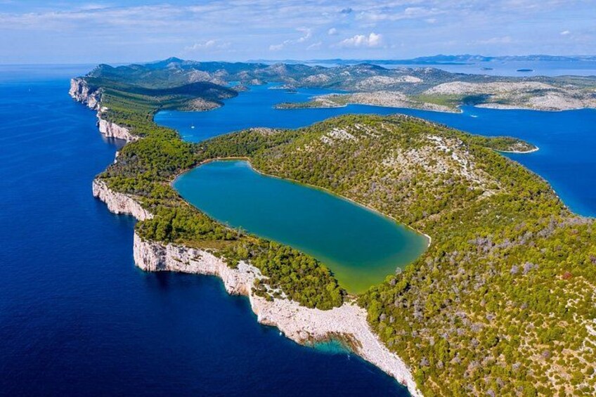 An aerial view of a coastal landscape with a large body of water, a narrow land bridge, and surrounding hills. 1
