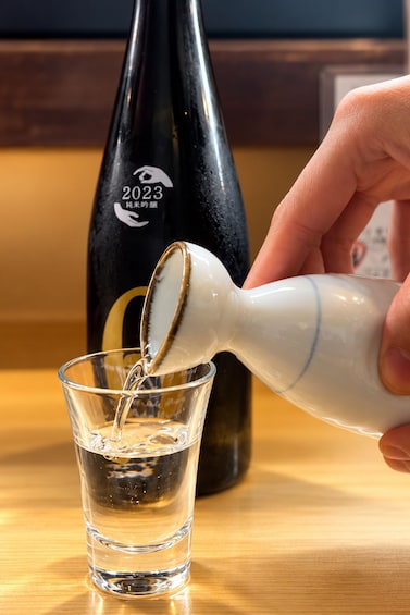 Une main verse un liquide transparent d’un flacon blanc dans un verre. 3
