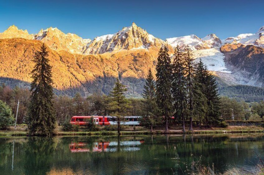 A lake with a red train, snow-capped mountains, and evergreen trees. 4