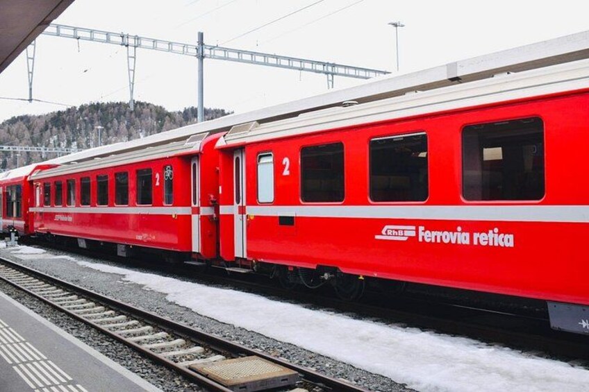 A red train with the number 2 on its side, parked at a station with snow on the ground. 2