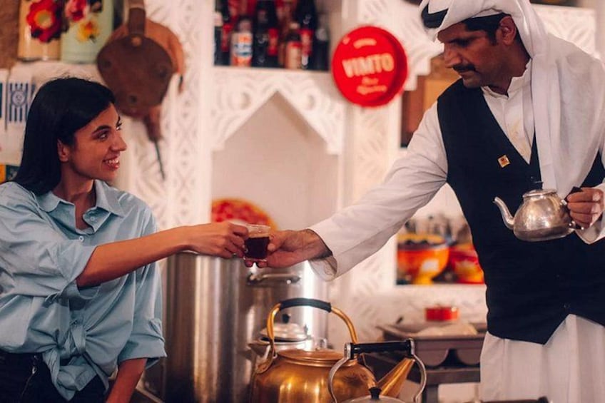 Una persona sirve té a otra en una cocina, con un hervidor y un samovar. 1