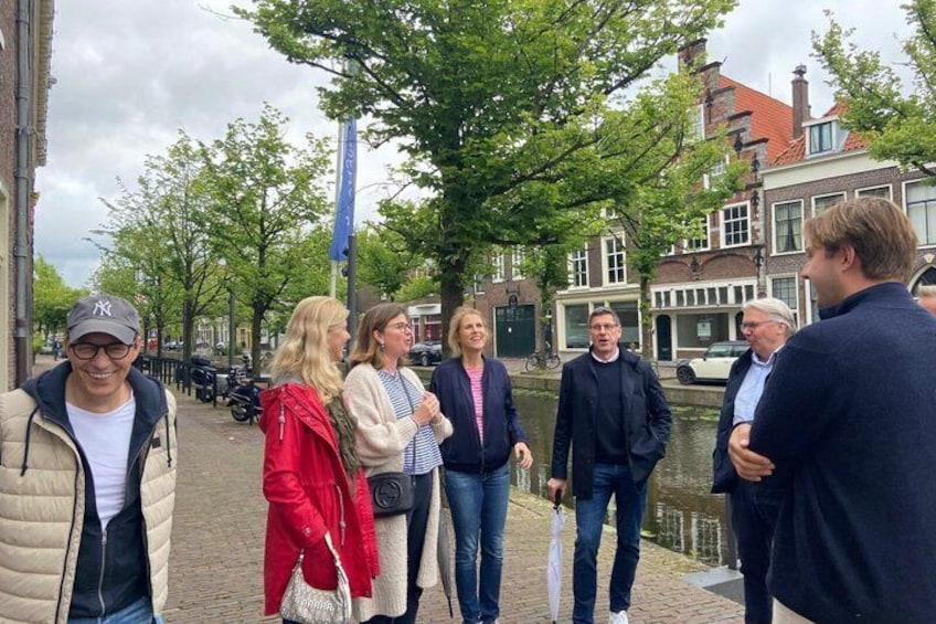 En gruppe mennesker står på en brostensbelagt gade ved en kanal i en historisk by. 3