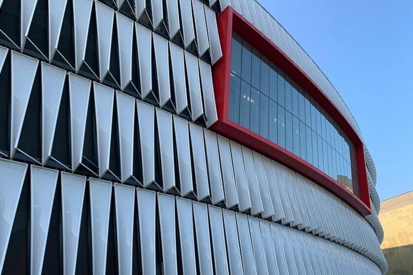 En byggnad med en unik, geometrisk fasad och ett stort, böjt fönster med en röd ram. 3