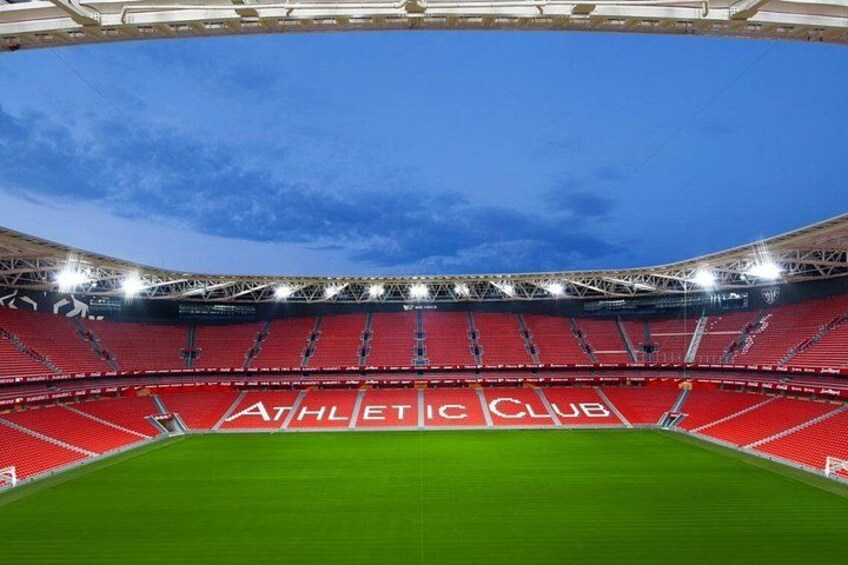 En stadion med röda sittplatser och en grön gräsmatta. 1
