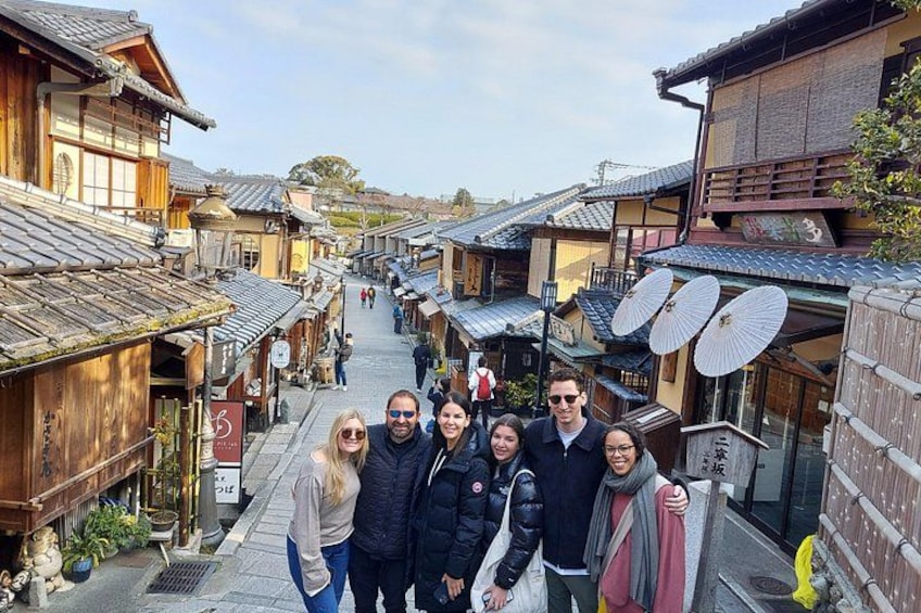A group of people standing in a traditional Japanese street with wooden buildings and tiled roofs. 1