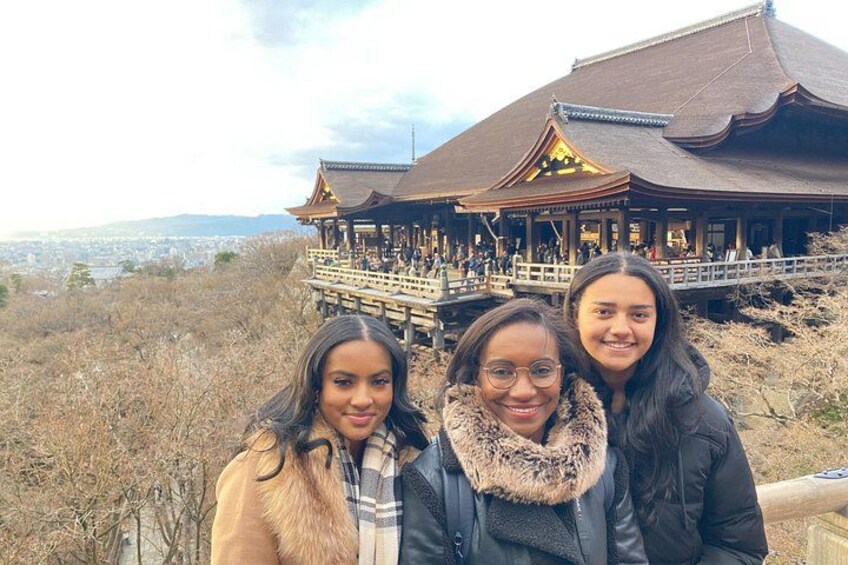 Three people standing in front of a traditional building with a wooden structure and a view of a city in the background. 5