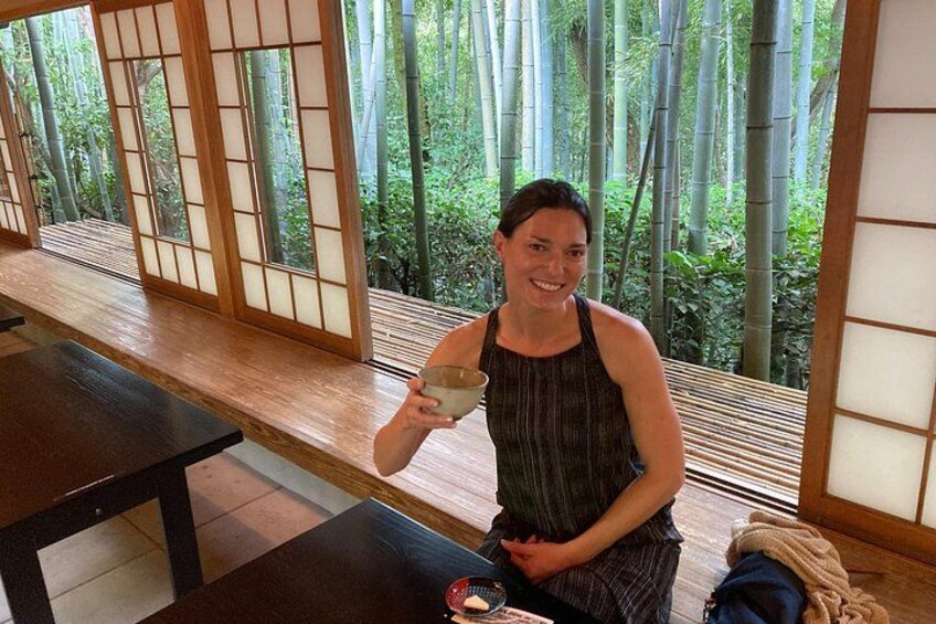 A person sitting at a wooden table in a room with large windows, holding a cup. 3