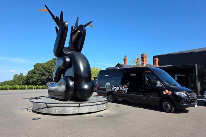 Una camioneta negra con la leyenda 'Local Way Tours' en su lateral estacionada junto a una escultura negra que se asemeja a un conejo. 3