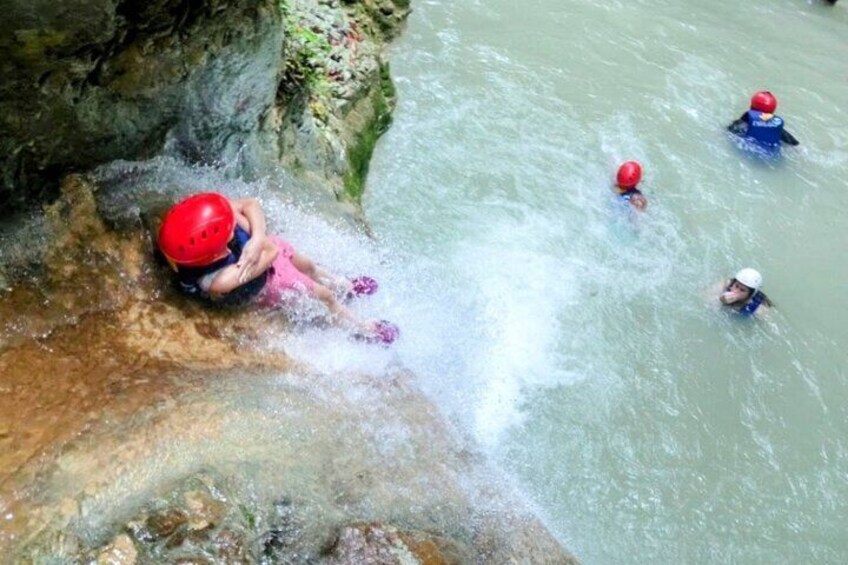 Une personne portant un casque rouge escalade une falaise rocheuse pour descendre vers une rivière. 5