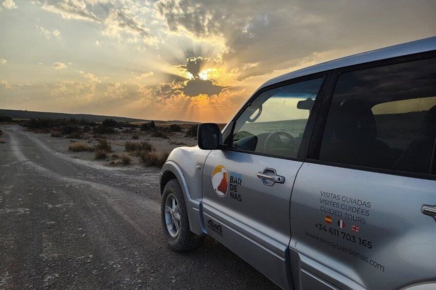 A silver SUV parked on a dirt road with a sunset in the background. 1