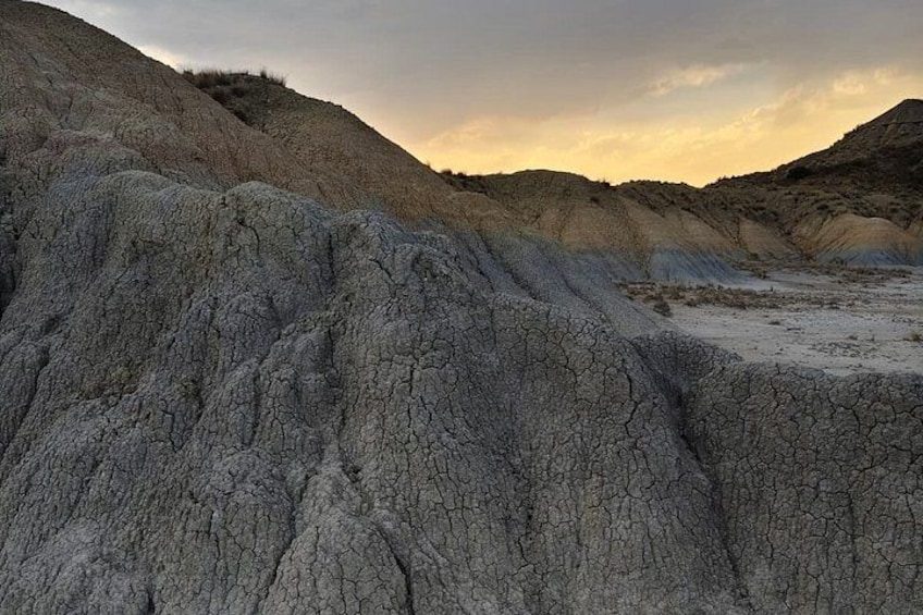 A dry, cracked landscape with layered hills and a cloudy sky. 2