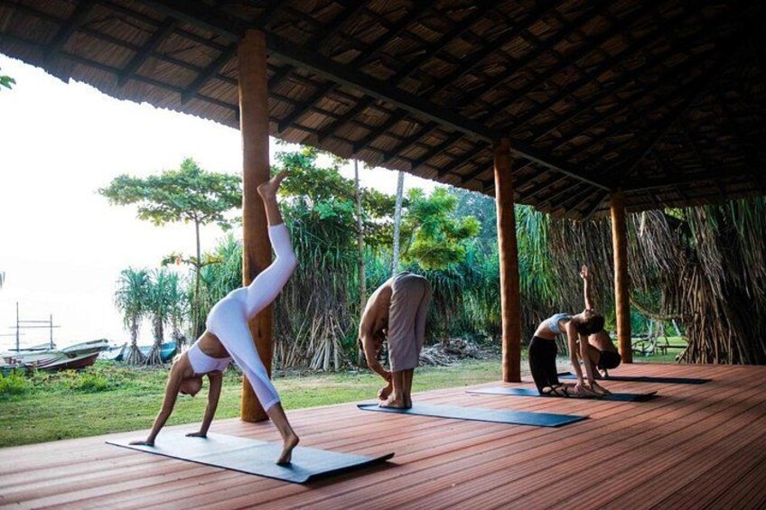 Three people practicing yoga on mats under a wooden shelter with a view of the sea and greenery. 4