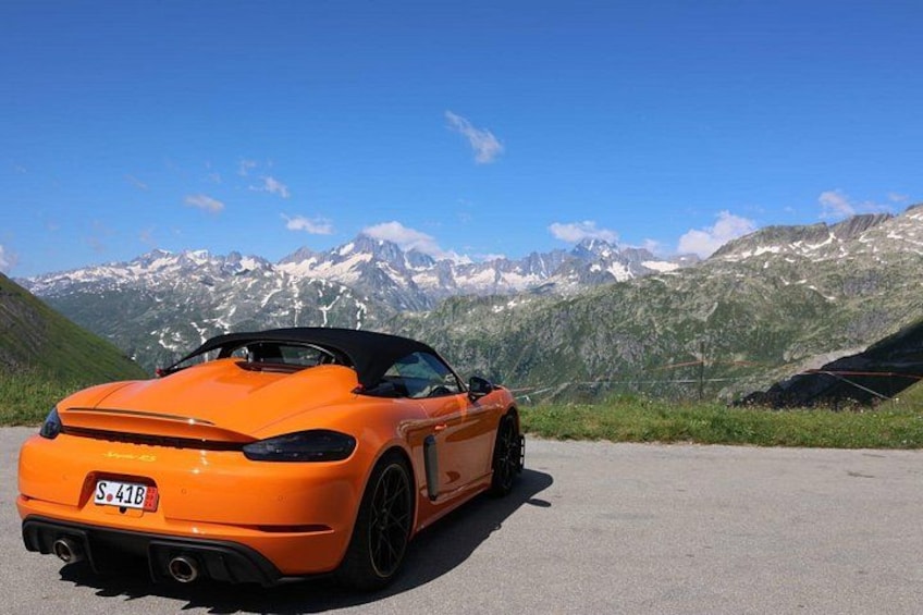 An orange convertible sports car parked on a road with a mountainous landscape in the background. 1