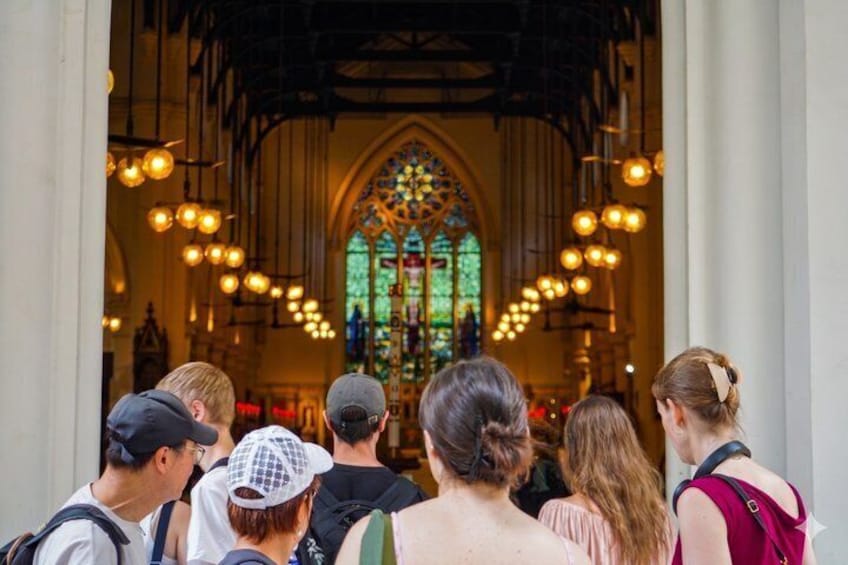 A group of people inside a church with a large stained glass window and hanging lights. 4
