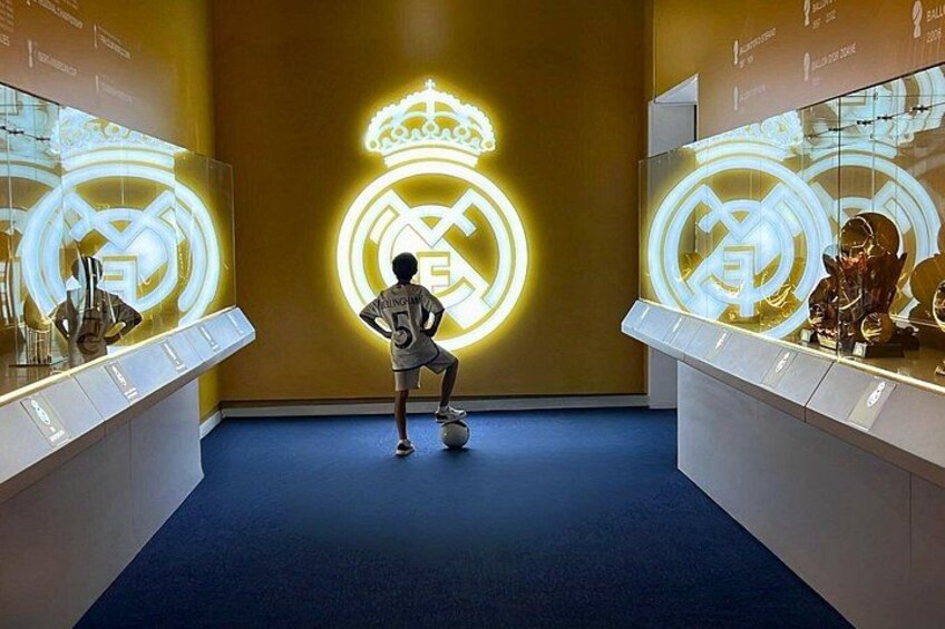 A person in a sports uniform practicing soccer kicks in front of illuminated Real Madrid logos. 3