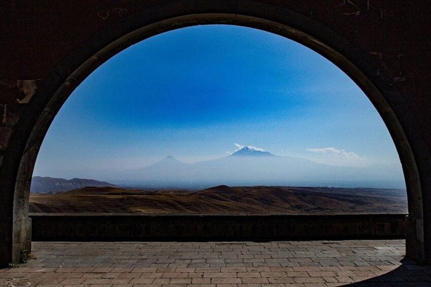 A view through an arched window of a mountainous landscape with a clear sky. 2