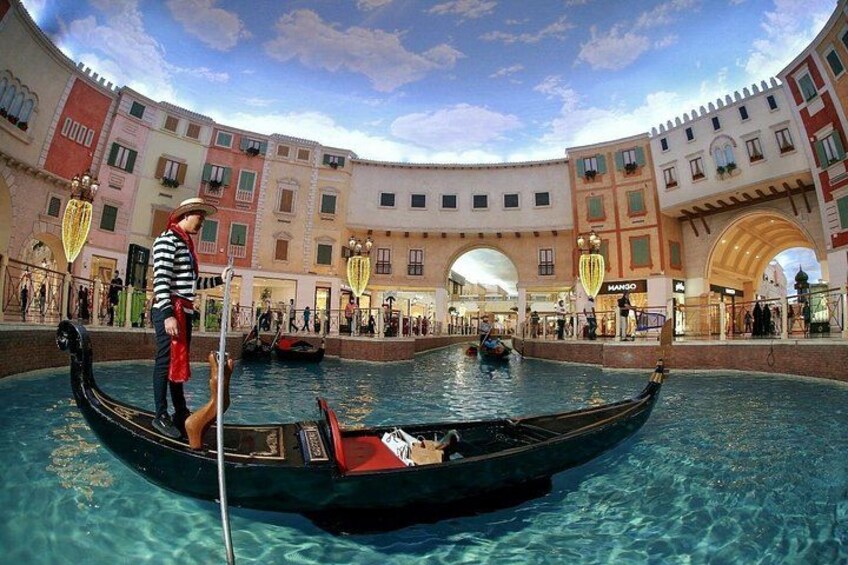 Una góndola navegando por un canal, con una persona de pie en ella, rodeada de edificios con ventanas de arco y balcones. 1