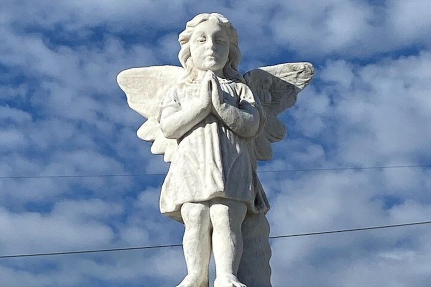 A statue of an angel with wings, standing against a sky with clouds. 4