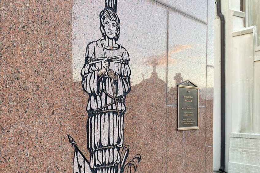 A sculpture of a woman on a granite wall, a plaque with text, and a building entrance. 3