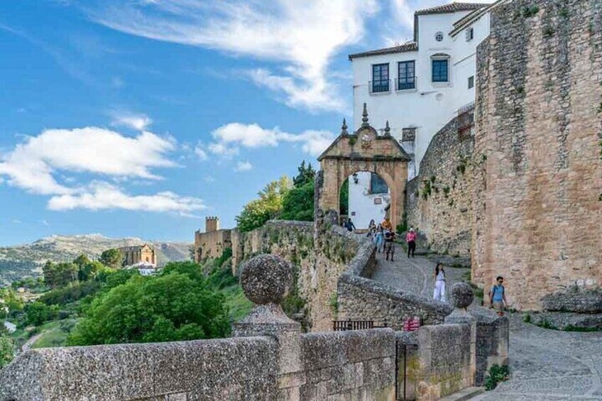 Un muro de piedra histórico con una puerta, un edificio blanco y una iglesia al fondo. 3