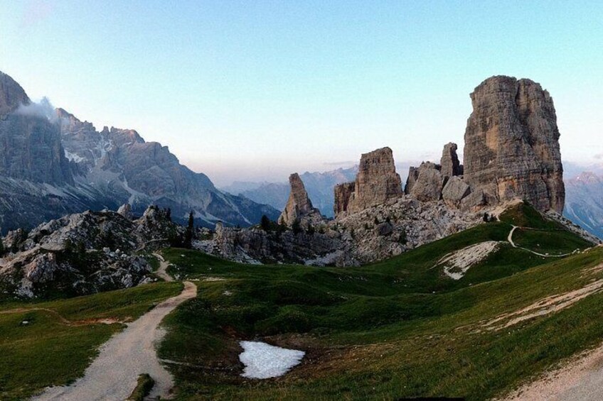 A mountainous landscape with a prominent rock formation, a dirt path, and a small pond. 1