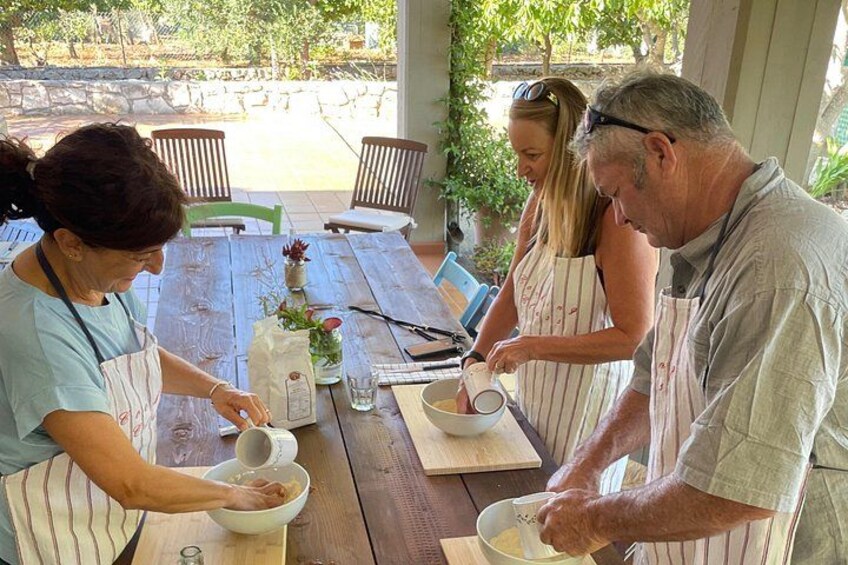 Four people preparing food outdoors at a wooden table with a garden view. 1