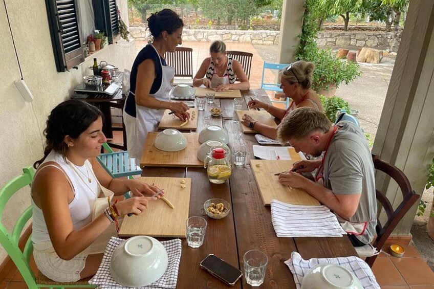 A group of people engaged in a cooking activity outdoors, with wooden tables and cooking utensils. 3