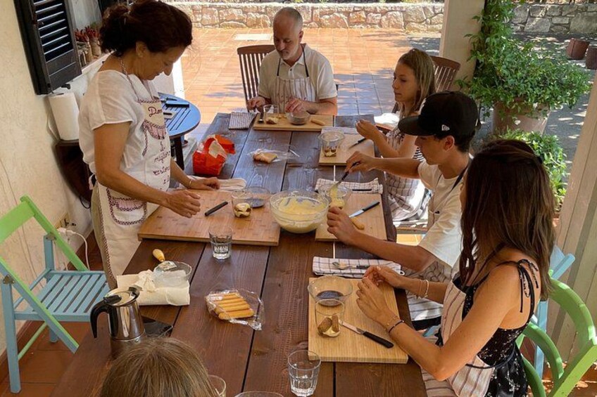A group of people preparing food outdoors at a wooden table with various ingredients and utensils. 2