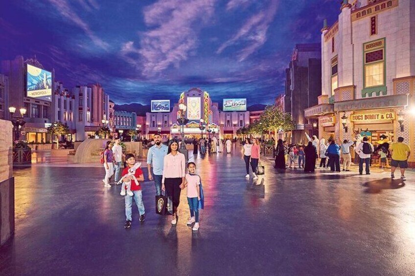 A bustling urban square at dusk with illuminated buildings and people walking. 3