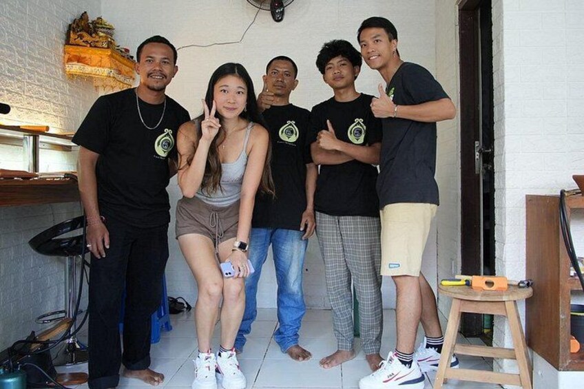 A group of people in a room with a white brick wall, a wooden stool, and a fan on the wall. 2