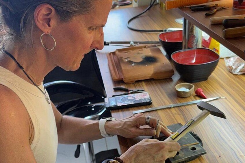 A person working with a tool on a wooden surface, surrounded by various objects like bowls and a cutting board. 1
