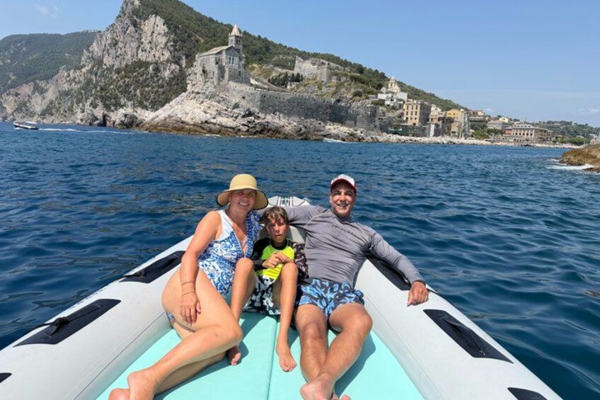 Tres personas en un bote, con un litoral rocoso y una iglesia al fondo. 2