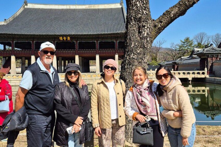 A group of people standing in front of a traditional building with a tiled roof and a pond in the background. 2
