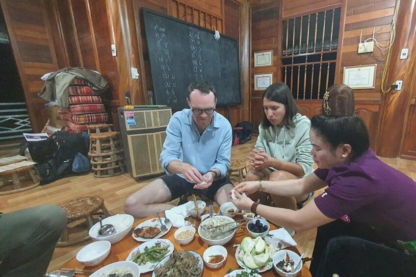 A group of people sitting around a table with various dishes, in a room with wooden walls and a blackboard. 2