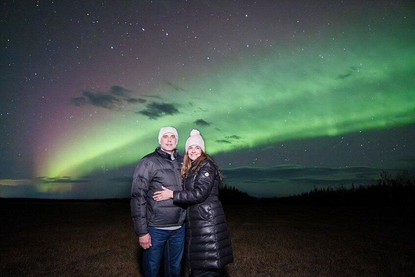 Two people standing in a field under a night sky with the aurora borealis. 3