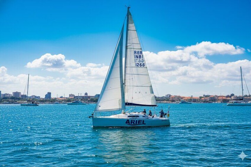 A sailboat named 'ARIEL' on a body of water with a cityscape in the background. 1