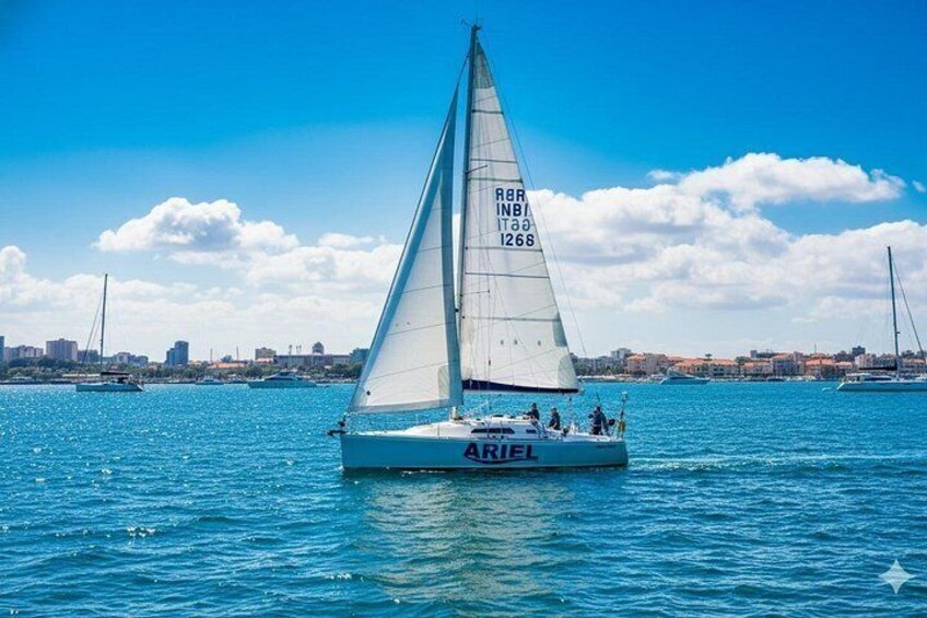 Een zeilboot genaamd 'ARIEL' op het water, met een stadszicht op de achtergrond. 1